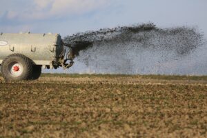 Ein landwirtschaftliches Fahrzeug düngt ein Feld, was zur Belastung des Grundwassers mit Nitrat führen kann.