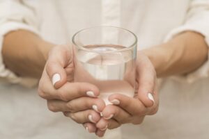 Eine Frau in einem weißen Hemd hält mit beiden Händen ein Glas mit klarem, reinem Wasser.