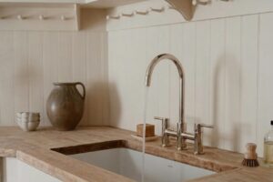 Eine helle Küche mit einer Arbeitsplatte aus Holz, in der klares Wasser aus einem modernen Wasserhahn in ein weißes Spülbecken fließt.